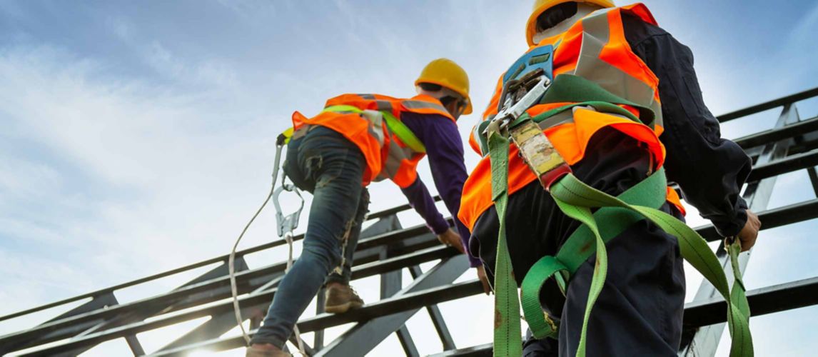 Two construction workers in protective gear working at height on a steel structure.
